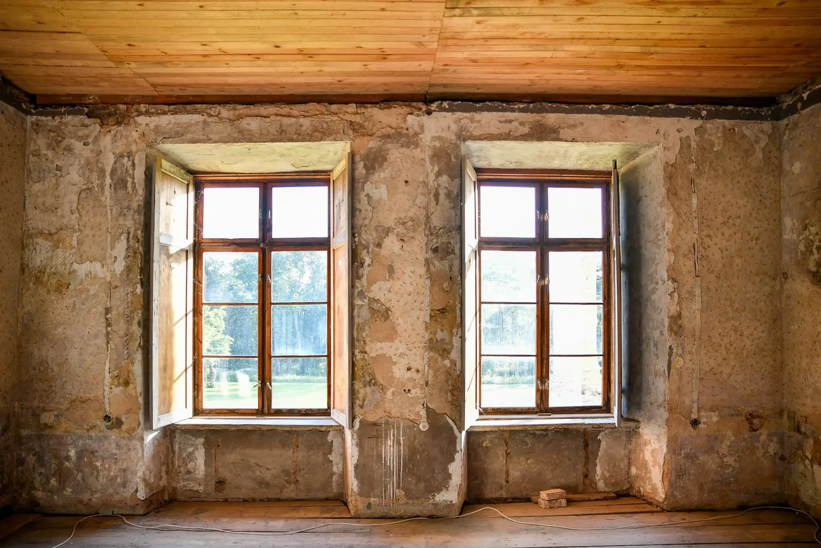 An old room with bare, patchy plaster and exposed brick before work started